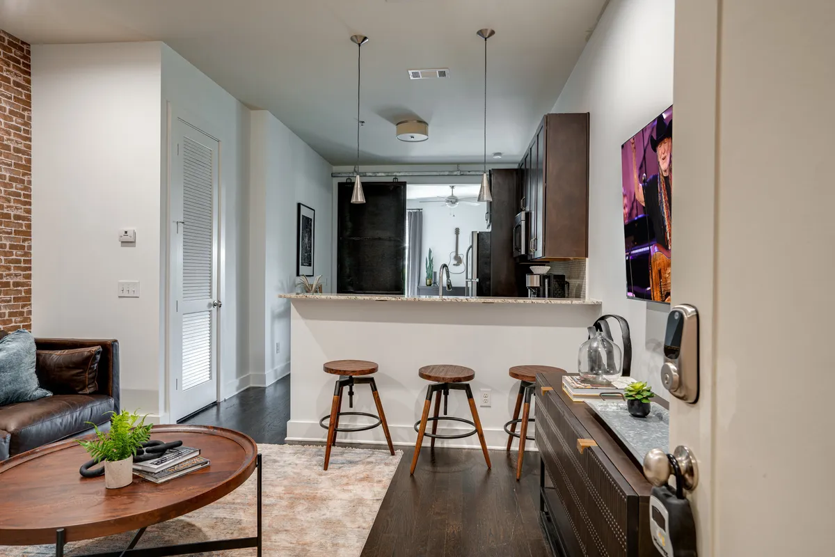 An inviting interior arrangement displaying a brick wall, kitchen island with bar stools, and a cozy coffee table setup. The layout is open, seamlessly connecting social spaces for gatherings, cooking, and relaxation.