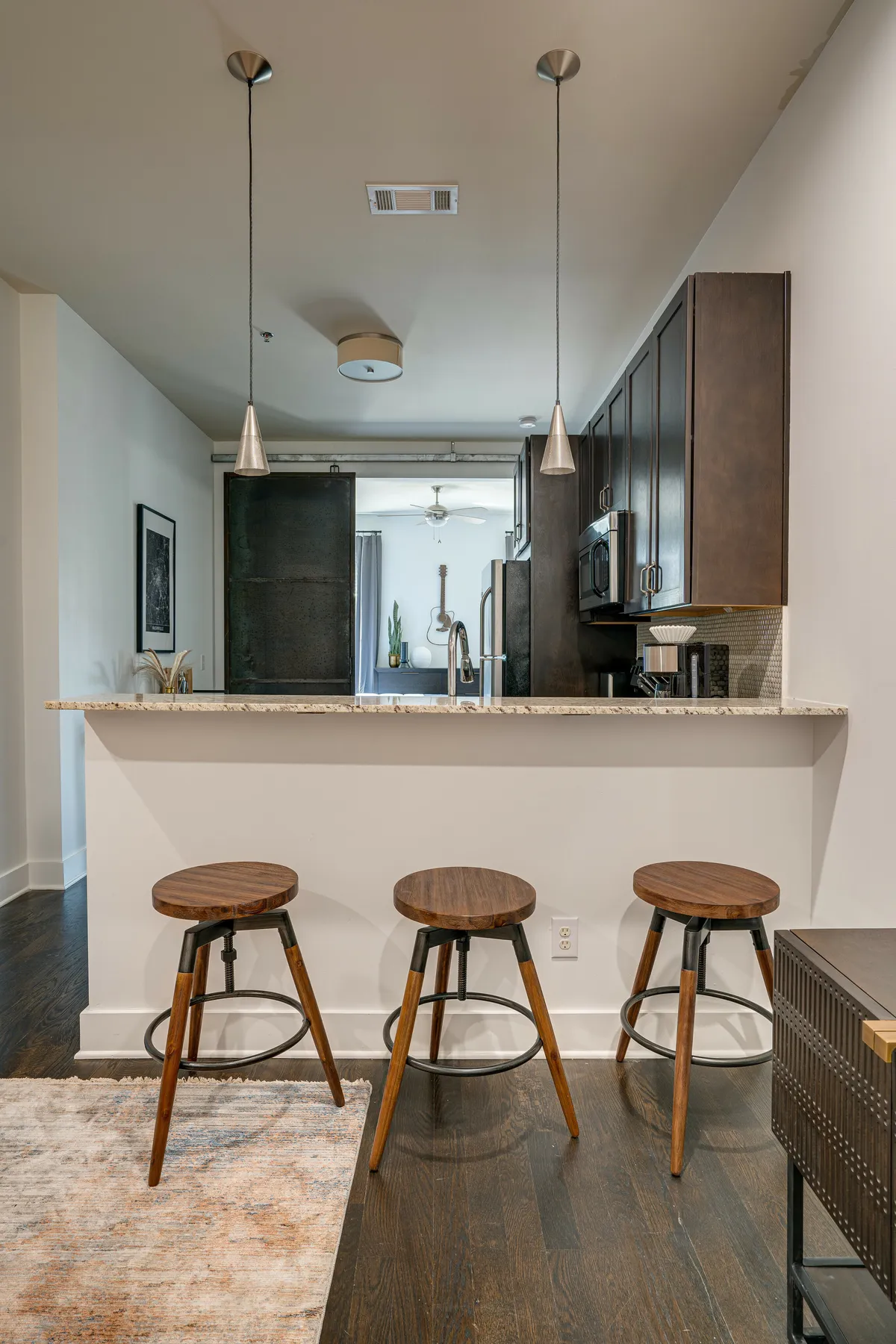 A modern kitchen bar with stools, pendant lighting above, a granite countertop, and dark cabinetry. The space looks inviting for both cooking and casual dining, with the bar area offering a spot for quick breakfasts, coffee, or socializing during meal prep.