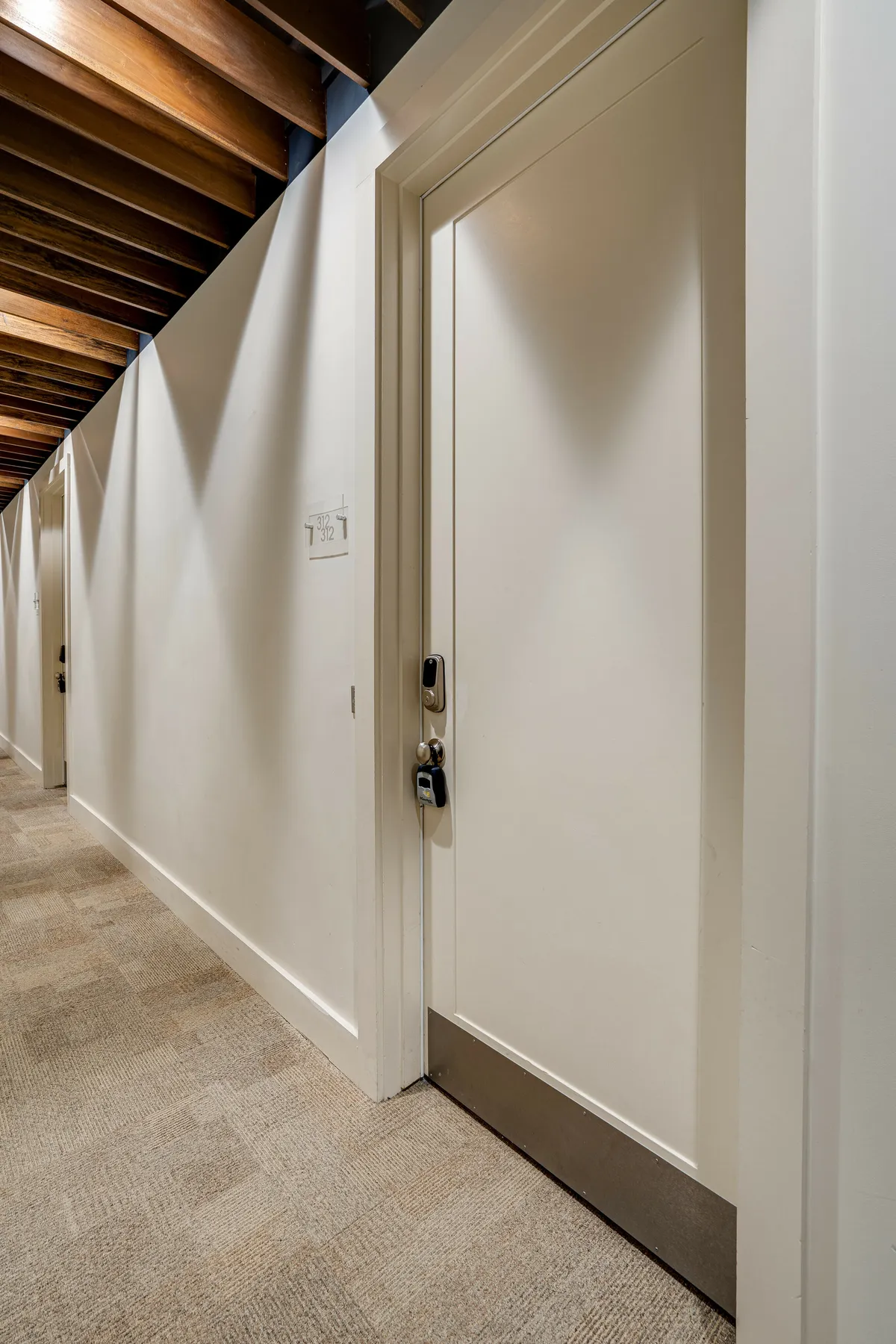 A simple hallway interior with a door, carpet, wall, and ceiling—suggesting common area access and the sense of secure, easy movement through the property, reminiscent of hotel-style check-in and elevator areas.